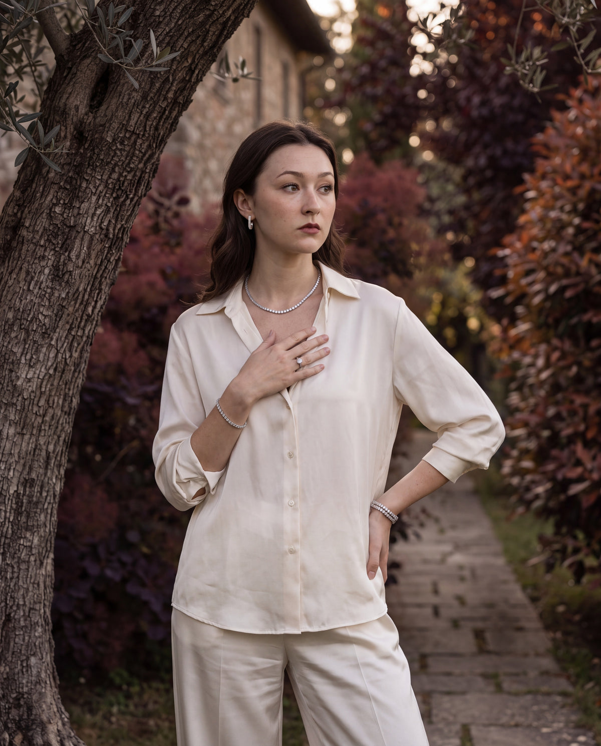 Tirzah pieces worn together on a garden path, including the round-cut tennis bracelet